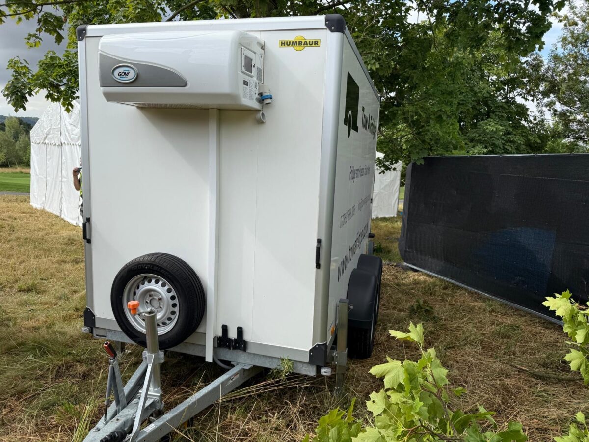 White trailer with air conditioning unit parked in a grassy area.